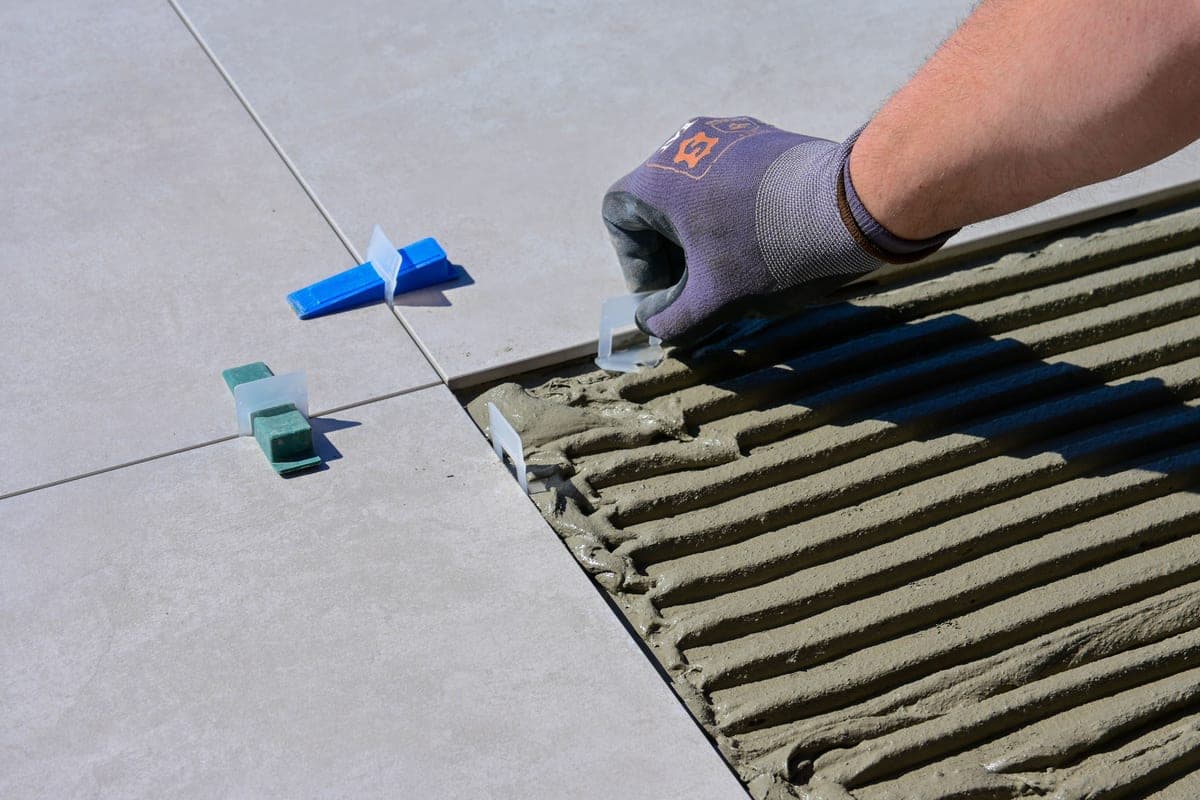 A tiler kneeling on a floor wearing knee pads while laying tile